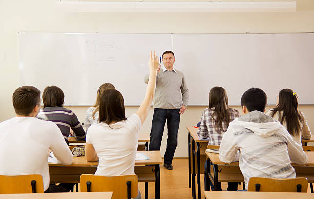 High-school students in classroom, girl responding to teacher's "Rear view of high-school students in a classroom, during lesson. Girl responding to teacher's question." teenage high school girl raising hand during class stock pictures, royalty-free photos & images
