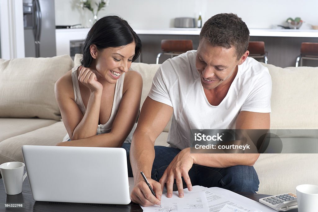 Couple doing paperwork with a laptop Couple doing paperwork with a laptop computer on the sofa Couple - Relationship Stock Photo