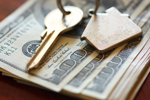 Set of house keys laying on hundred dollar bills stock photo