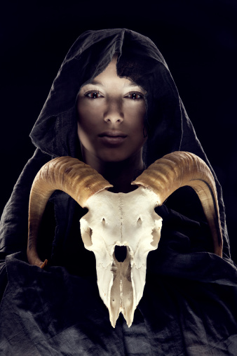 portrait woman in the hood with sheep's skull on black backround.