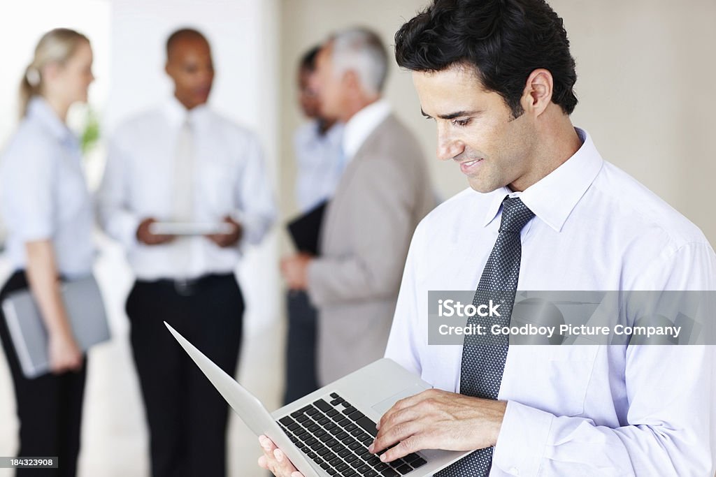 Business man working on laptop Portrait of handsome business man working on laptop with colleagues in background 30-39 Years Stock Photo