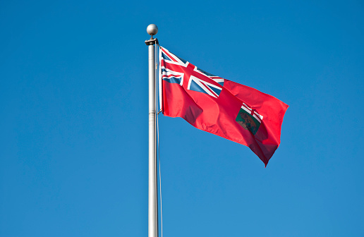 Waving flag of Manitoba, Canada, against blue sky