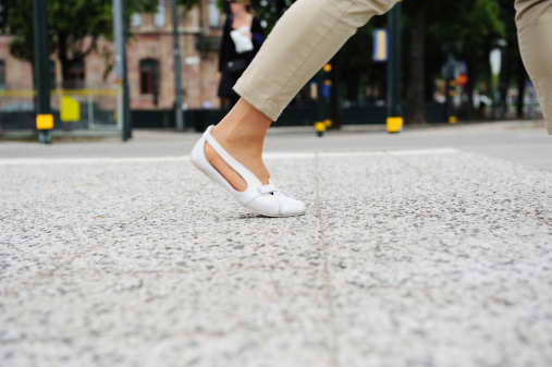Woman with white shoes walking on tiled sidewalk. Zebra crossing out of focus in background.