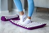 Close up of woman legs standing doing foot self health massage at home, acupressure mat therapy. Lady on orthopedic acupressure mat, legs massage. Home healthcare medical concept. Copy ad text space