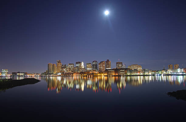 Moonlit night in Boston Downtown Boston Skyline along the Boston Harbor waterfront. Photo taken on a calm evening with a full moon in the  East Boston neighborhood. The Boston cityscape is a mixture of old and new buildings. Boston is the capital and largest city in Masssachusetts. Boston is the largest city in New England  east boston stock pictures, royalty-free photos & images