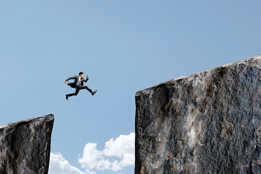 A businessman takes a leap of faith that he can accomplish jumping from one cliff to another cliff.