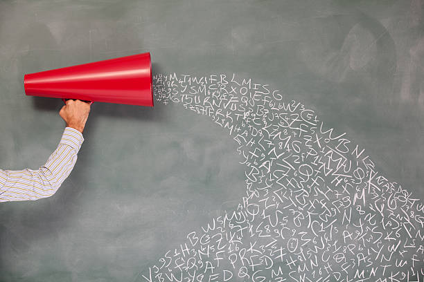 Letters coming out from a red megaphone on blackboard.The letters are written on blackboard word by word with chalk.The shirt color is less white just to get attention on red megaphone that is in man hand and located on left side of frame.Shot with a full frame DSLR camera.