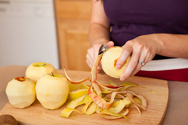 jeune femme éplucher des pommes en cuisine - épluché photos et images de collection