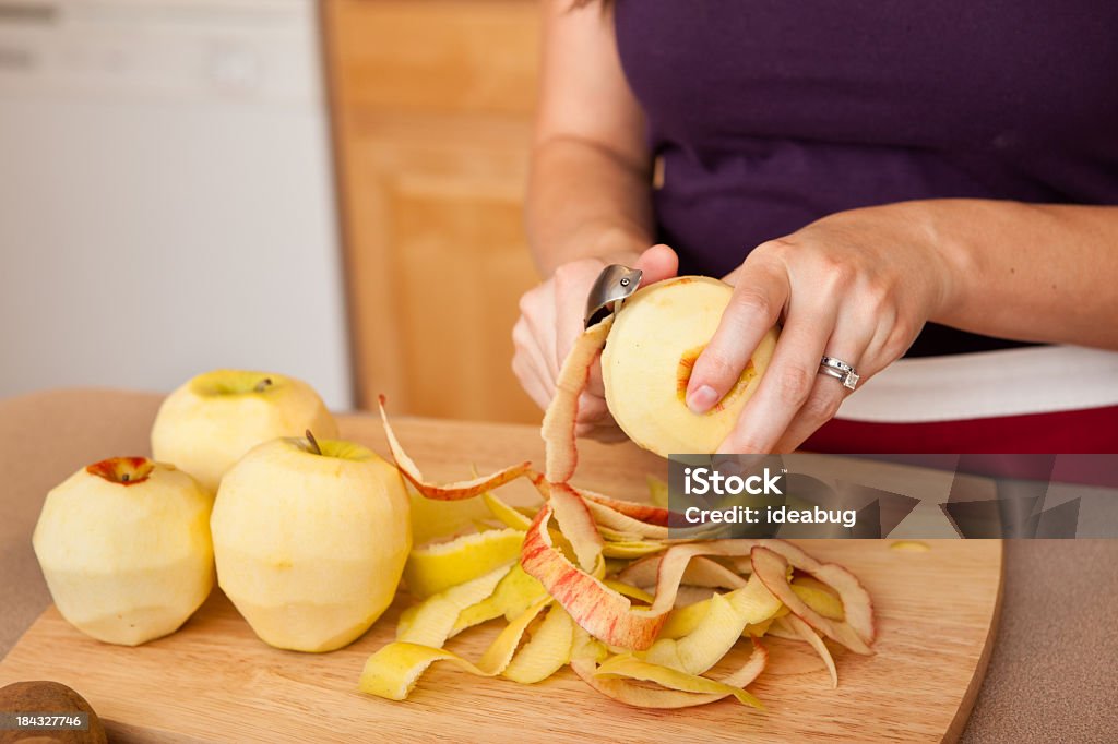 Young Woman Peeling Apples in Kitchen Color photo of a young woman peeling apples in her kitchen at home. Apple - Fruit Stock Photo