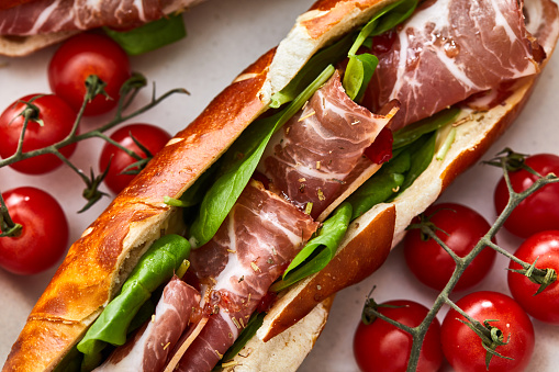 A perfect healthy meat sandwich, made from Bavarian bread bun, prosciutto, green salad, cherry tomato salsa, local organic seasoning, herbs and spices. Representing a healthy lifestyle, healthy eating, a wellbeing, modern city life, street food culture and a perfect brunch gourmet delicatessen.