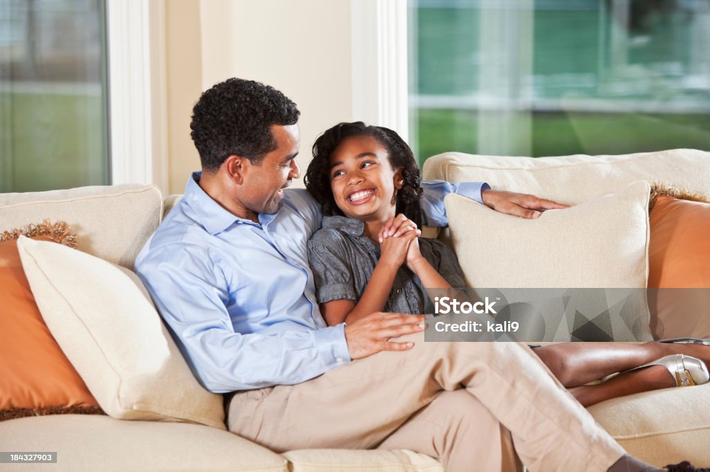 Excitación Chica con padre en el sofá hablando - Foto de stock de Afrodescendiente libre de derechos