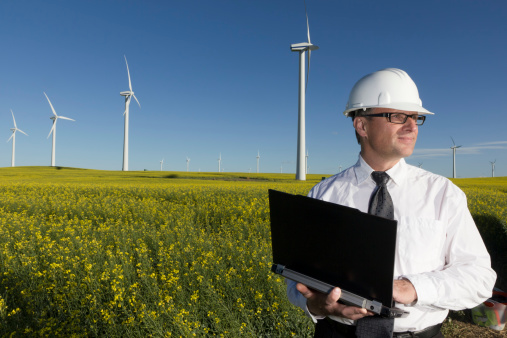 An image from the alternative energy industry of an engineer and laptop at a wind farm.
