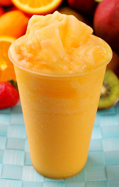 Orange slush in plastic glass with fruit in the background