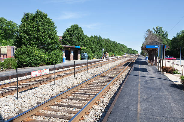 Railway tracks extend towards the horizon during golden hour, capturing the serene atmosphere of a train station in daytime. Tracks are flanked by lush greenery.