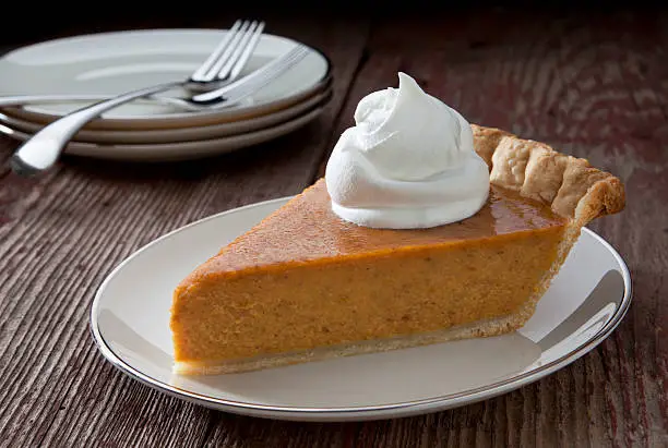 Photo of Pumpkin Pie slice with whipped cream on a rustic table.