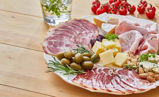 Charcuterie luxury. A perfect holiday appetizer plate, made from variety of ham and cheese delicatessen, dry beef ham, dry pork sausage, Camembert cheese, Gauda cheese, organic olives, dry figs, cherry tomato, rosemary, fresh olive oil, local organic seasoning, herbs and spices. Representing a healthy lifestyle, healthy eating, a wellbeing, modern city life, traditional culture and a perfect brunch gourmet delicatessen.
