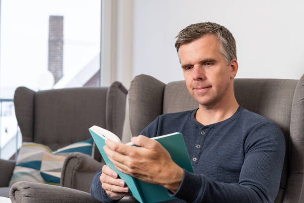 istock handsome 40s single man sits in an comfy  grey armchair and reads 1843339297