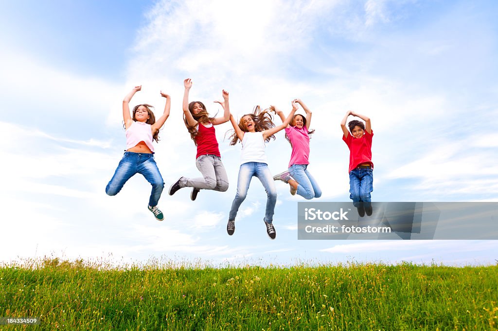 Group Of Happy Chilldren Jumping Outdoors Group of happy elementary age children jumping outdoors in the field against blue sky. Activity Stock Photo