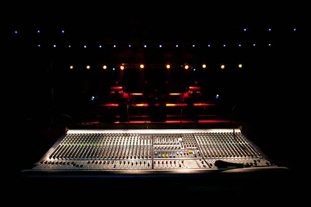 Lights illuminate a concert stage prior to a concert with a sound mixer in the foreground.