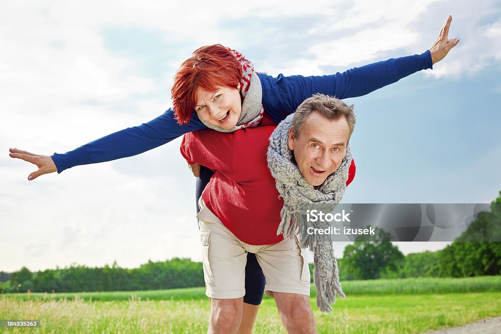 Piggyback An attracitive, happy mature man piggybacking his laughing wife against blue sky in the countryside. Active Seniors Stock Photo