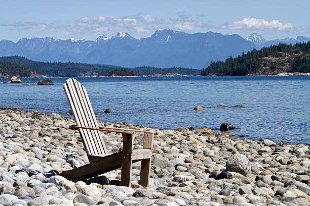 Adirondack chair on rocky oceanfront beach with mountains