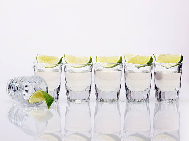 Six tequila shots on a white background Row of Tequila Shot glasses with lime and salt. One down, five to go! tequila slammer stock pictures, royalty-free photos & images