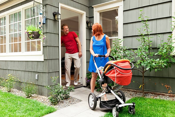 Young Family Leaving Home with Baby Stroller Photo of a young family on their way out to take a walk with their new baby in a stroller; husband is shutting the door behind him. blue house red door stock pictures, royalty-free photos & images