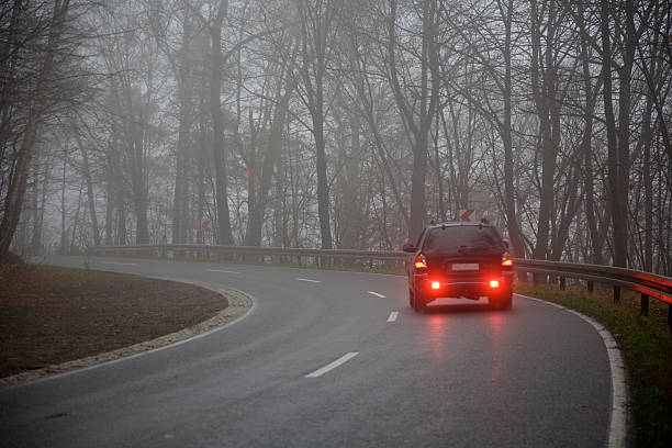 Picture of a car on the road on a gray day car driving through the fog on a wet road tail light stock pictures, royalty-free photos & images