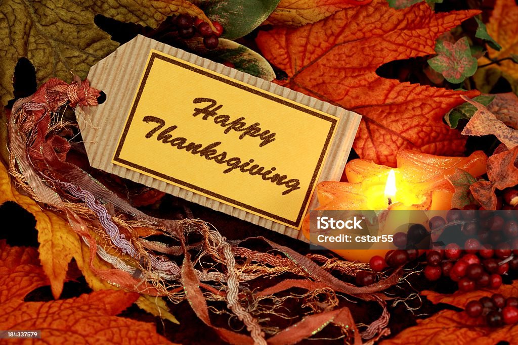 Holiday: Happy Thanksgiving on tag with leaves Still Life Happy Thanksgiving still life with tag that says happy thanksgiving and multicolored tassels. autumn leaves, berries and candle surround the tag. Thanksgiving - Holiday Stock Photo