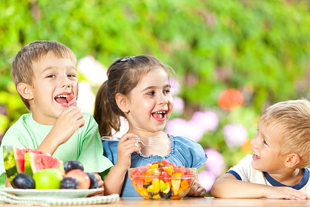 Group of small children having healthy snack, eating fresh fruit salad outdoors.