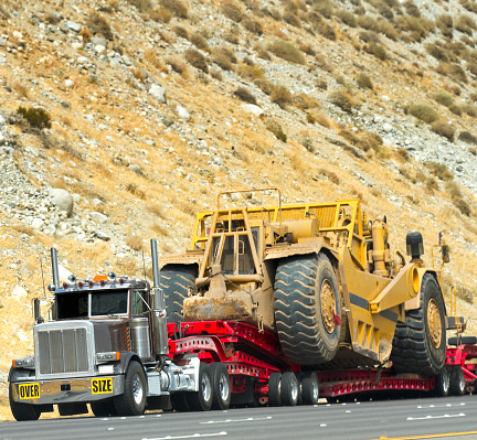 A semi truck hauls a large earthmover down the road.