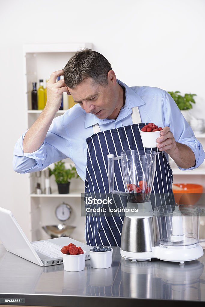 Hombre maduro concentrarse mientras usando computadora portátil durante la preparación de la comida - Foto de stock de 50-59 años libre de derechos