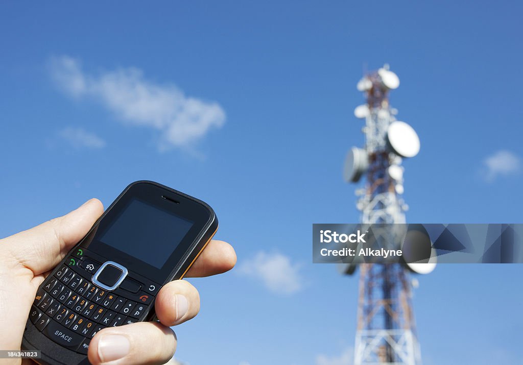 Sosteniendo un teléfono móvil y una torre de comunicación - Foto de stock de Agarrar libre de derechos
