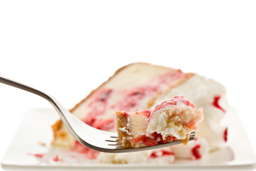 A close up of a bite of strawberry cheesecake on a fork with the rest of the cheesecake out of focus in the background. Isolated on white.