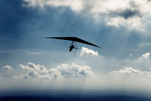 Hang glider against dramatic sky. Sun-rays coming out from the clouds.