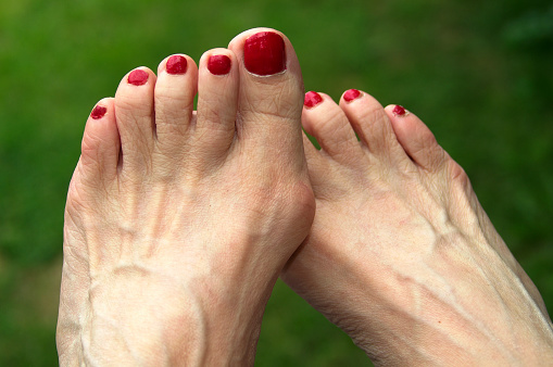 Beautiful female feet with pedicure nails, red gel polish, glitter design