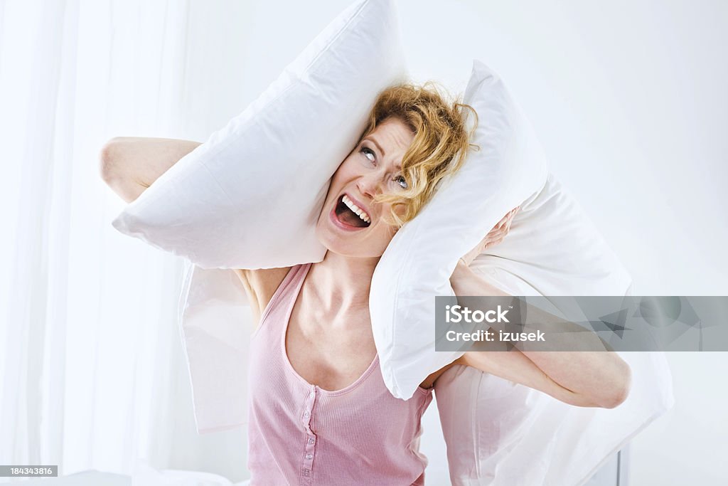 I can't sleep!! Young adult woman squeezes pillows to her ears and screaming, can't sleep because of a big noise. 25-29 Years Stock Photo