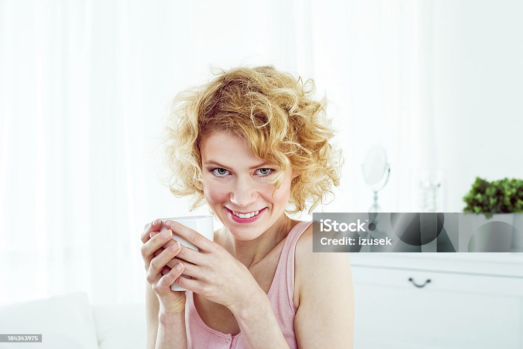 Morning caffee Pretty young adult woman wearing pink sleeveless top holding cup of coffee in the morning, looking at camera and smiling. 20-24 Years Stock Photo