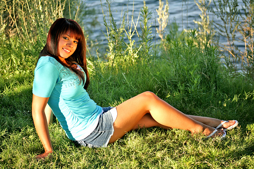 Beautiful Hispanic girl seated in the grass by the river.