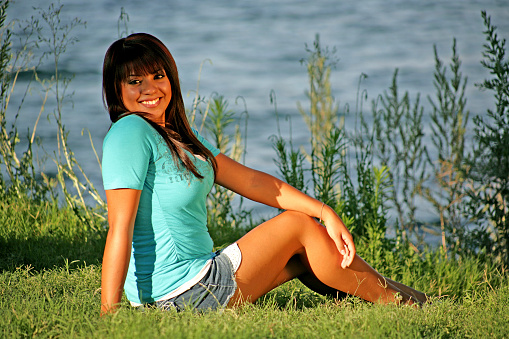 Beautiful Hispanic girls seated on the grass by the water.