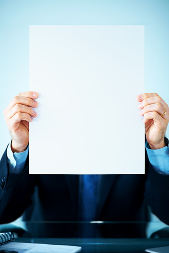 Portrait of a businessman sitting in office holding a blank sign in front of his face