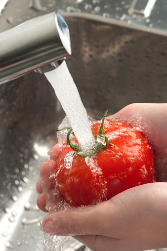 Womans hands washing a tomato under running water