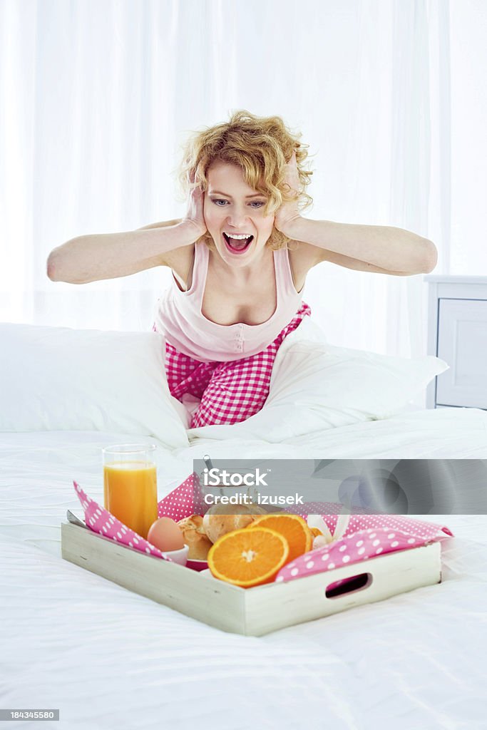 Surprise in the morning Surprised young adult woman with hands covering ears looking at the breakfast tray served to her bed. 25-29 Years Stock Photo