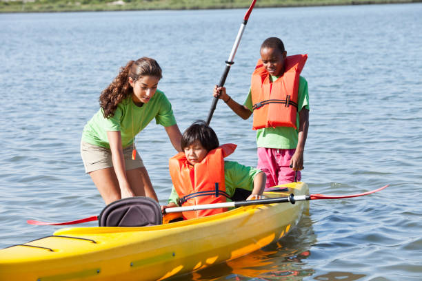 adolescente ajudar os rapazes com caiaque - summer camp child teenager kayak - fotografias e filmes do acervo