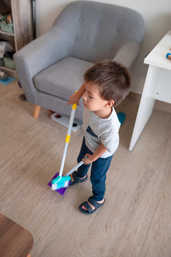 Witness the charm of a two and a half year old boy joyfully sweeping the floor at home. Encourage early learning and responsibility with this heartwarming image of a little helper in action