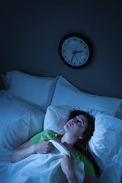 Sleepless Insomnia Woman Waking in Stress and Anxiety in Bed "Subject: Young woman having insomnia, trouble falling asleep, awake as time passes on clock" insomnia stock pictures, royalty-free photos & images