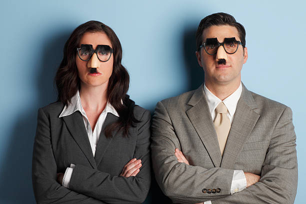 Teamwork A businessman and a businesswoman standing with arms folded while wearing Groucho Marx glasses. groucho marx disguise stock pictures, royalty-free photos & images