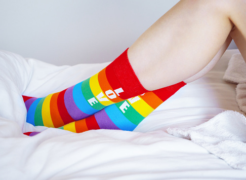 Woman wearing rainbow socks lying on the bed at home. Rainbow stripes as a modern sign of the LGBT community