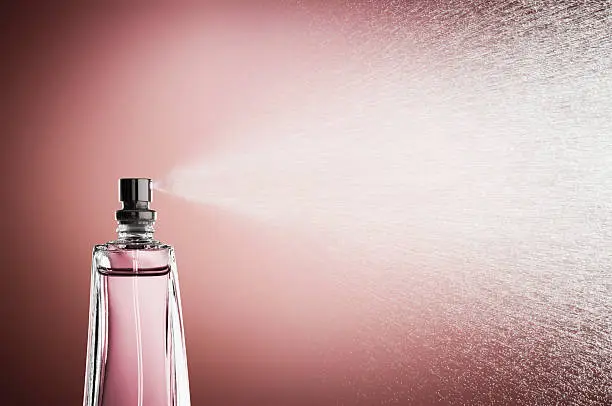 Photo of Glass bottle of perfume spraying mist against pink background