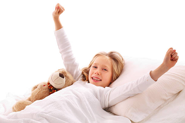 a little cute baby girl on a white cotton bed at home with a soft toy in her hands smiling on the bed at home